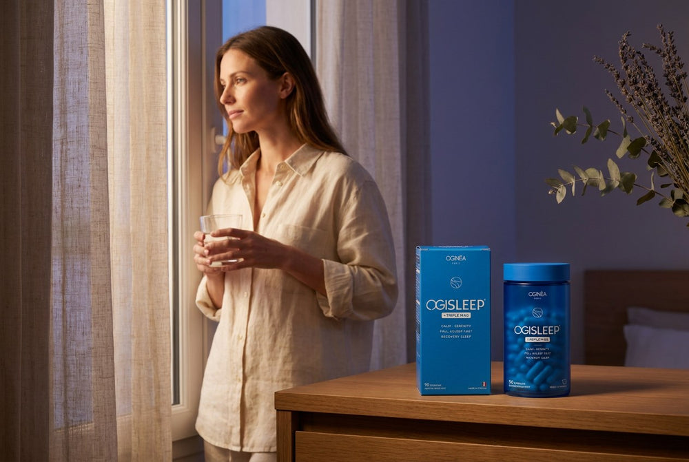 A woman drinking water while holding an OGISLEEP bottle in the evening